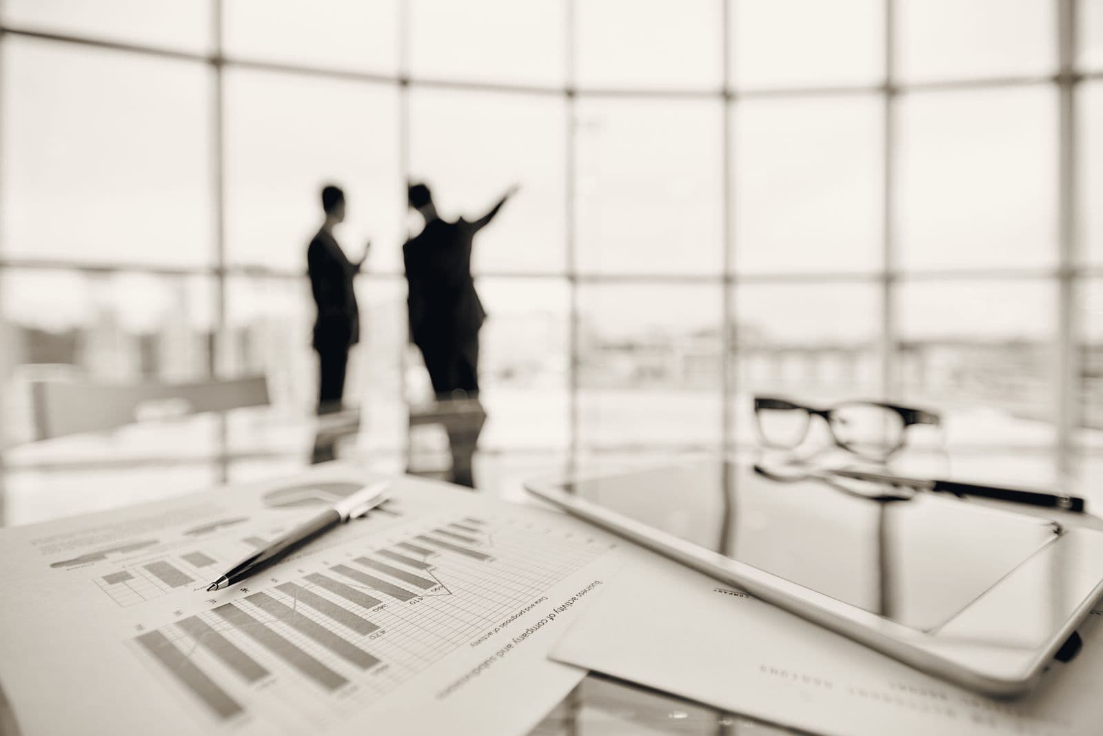 Two advisers in conversation by a window, business planning documents in the foreground.